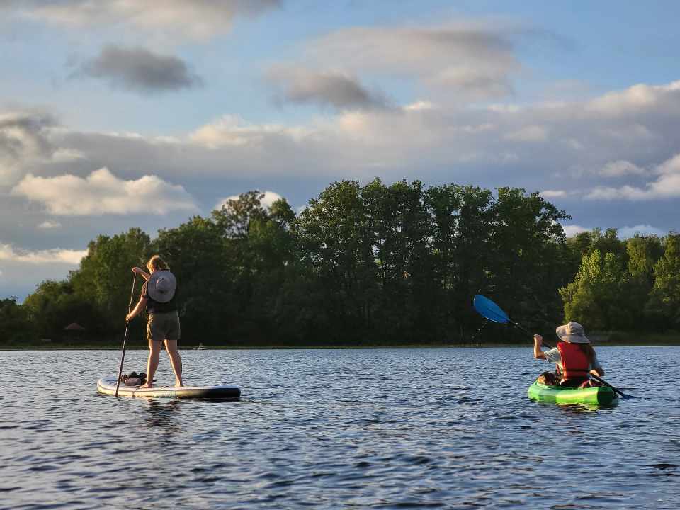 person standing on paddleboard and kayak on right on water